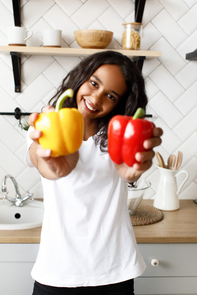 Smiling girl holding up yellow and red peppers